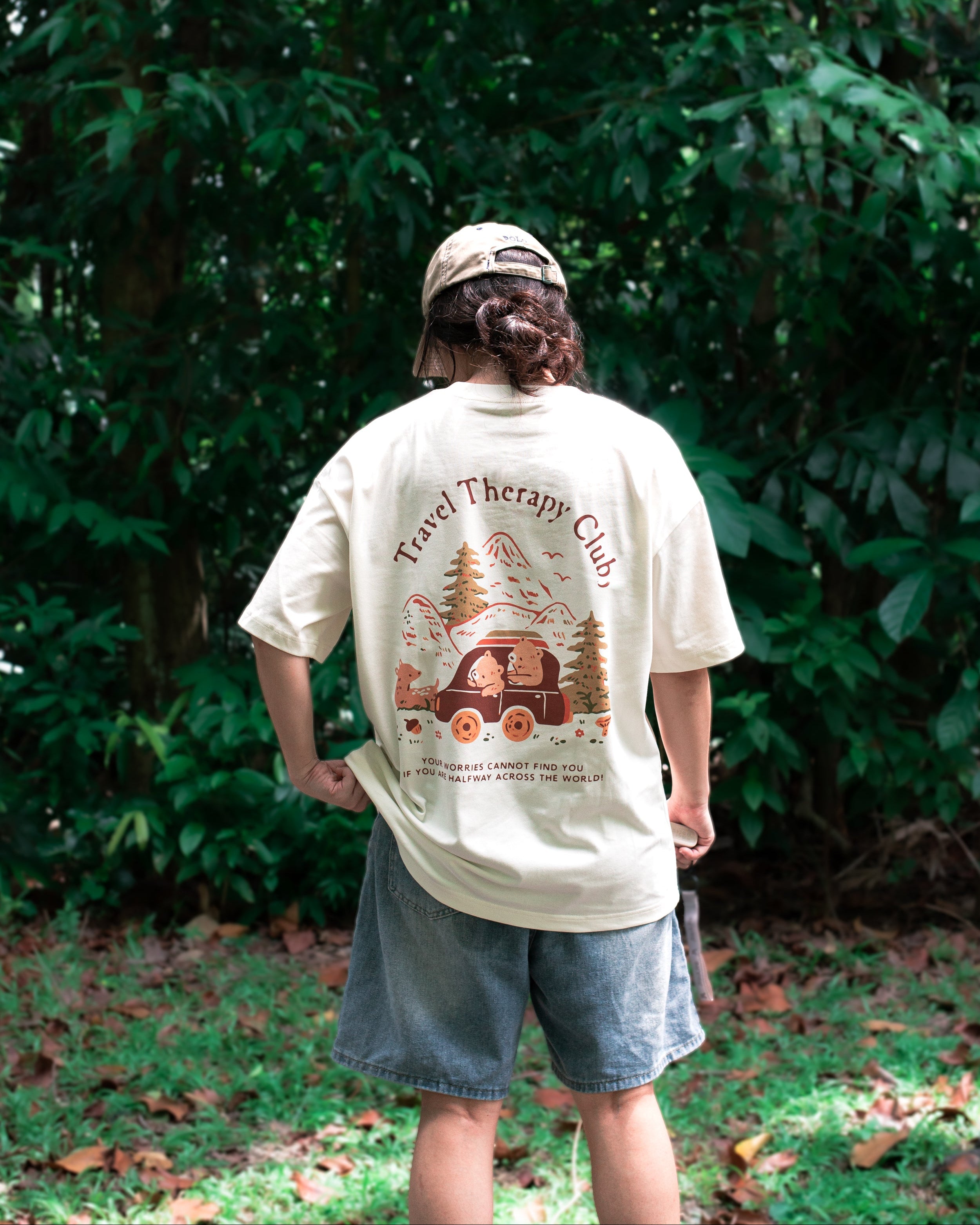 Person wearing a 'Travel Therapy Club' t-shirt with a graphic design outdoors.