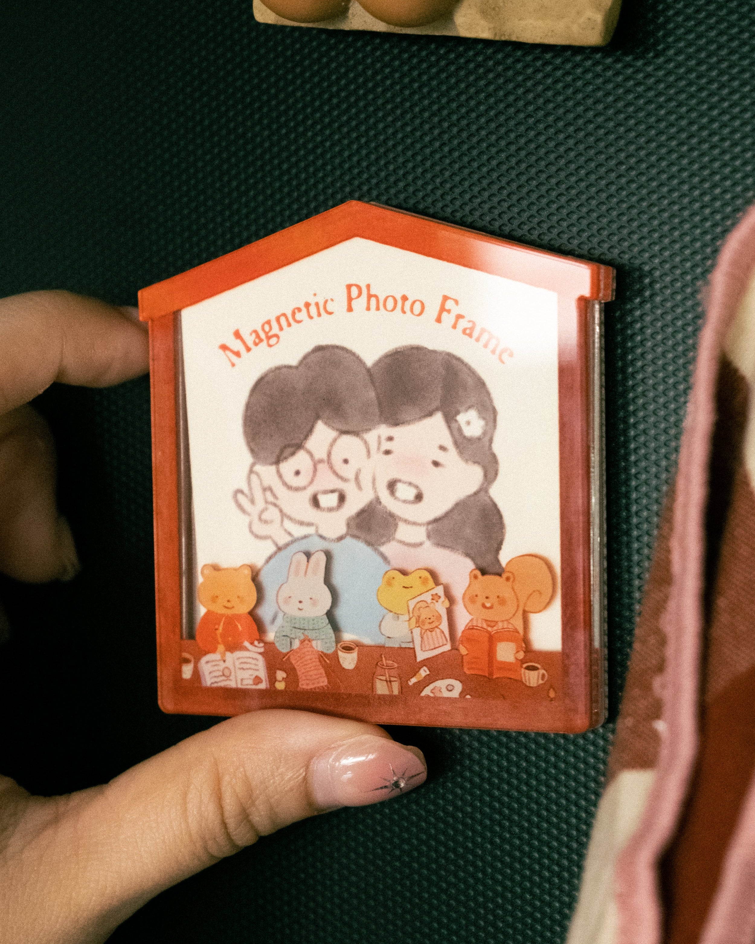 Magnetic photo frame with cartoon design held by a hand on a dark surface.