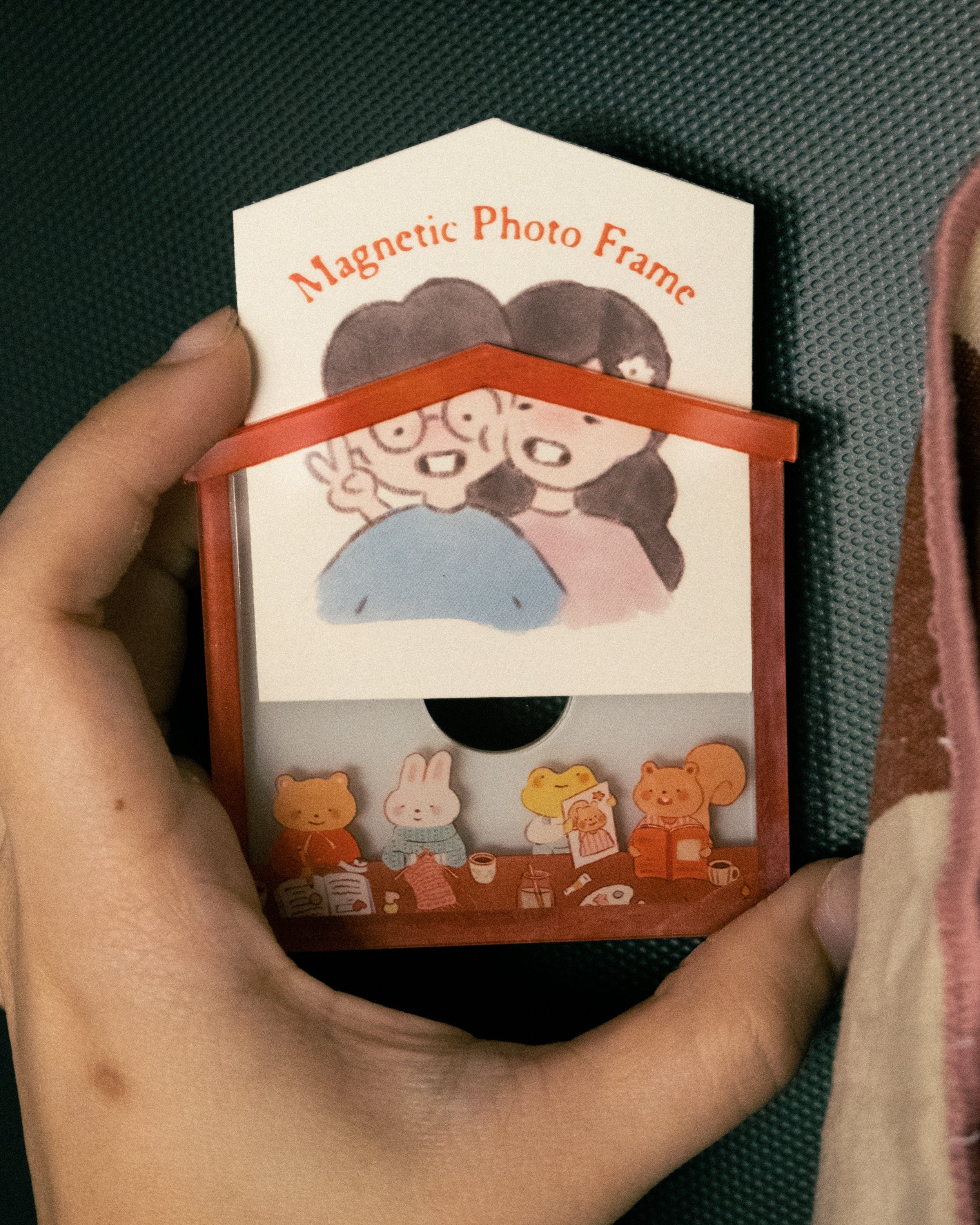 Hand holding a magnetic photo frame with cartoon characters on a textured surface