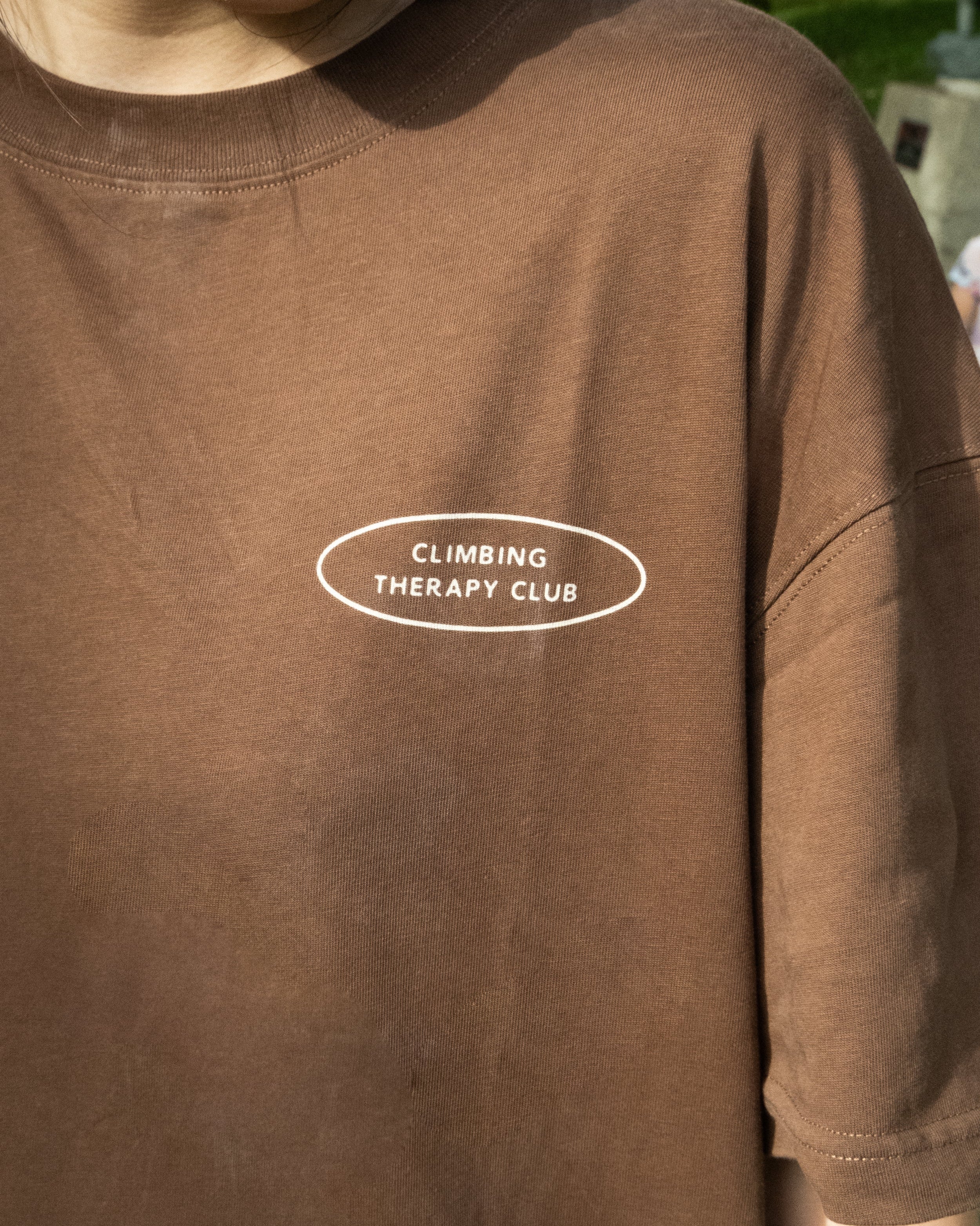 Brown t-shirt with 'Climbing Therapy Club' text on a person wearing it.